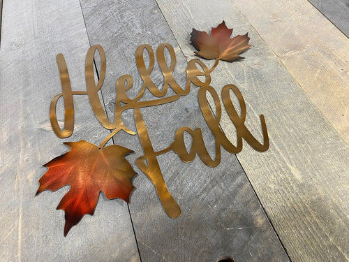 Decorative metal sign with 'Hello Fall' text and autumn leaves on a wooden surface