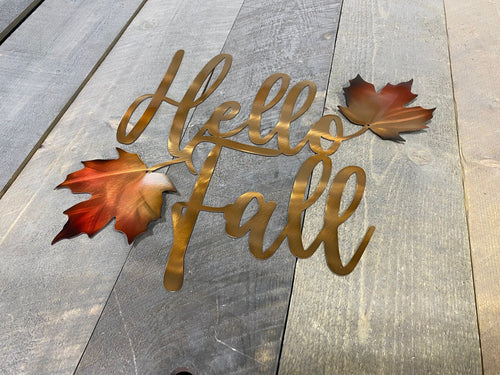 Decorative metal sign with 'Hello Fall' text and autumn leaves on a wooden surface