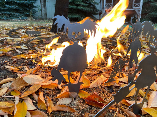 Silhouettes of skeletons and a cat around a campfire with autumn leaves on the ground.