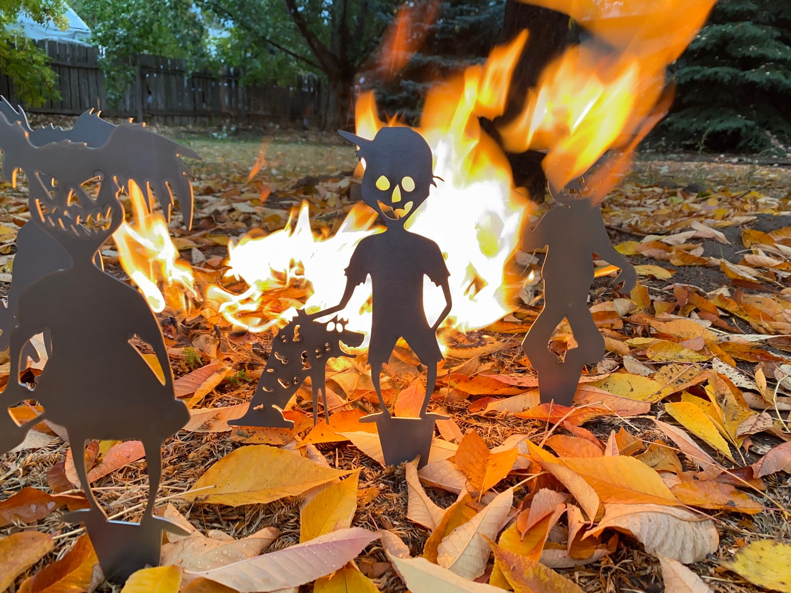 Silhouettes of people around a bonfire with autumn leaves on the ground