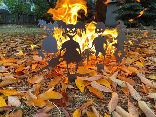 Silhouettes of Halloween figures in front of a fire with autumn leaves on the ground.